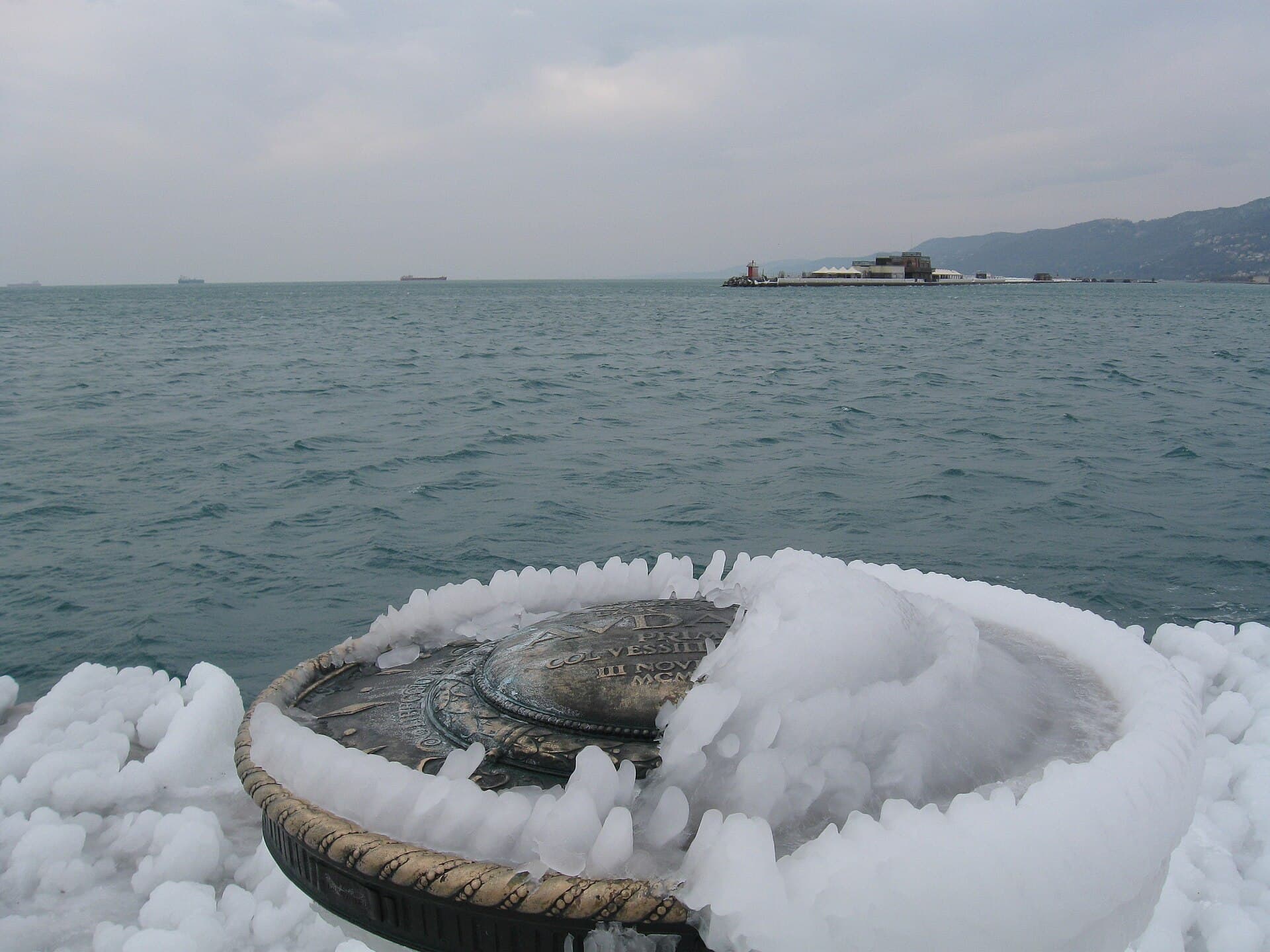 The bronze compass rose of the Molo Audace covered in ice, with the winter Adriatic behind